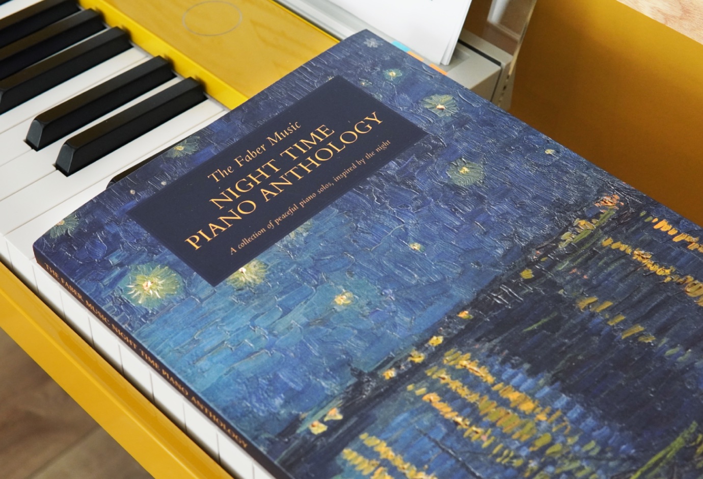 A photo of a piano music book laid down on the keys of a yellow digital piano.